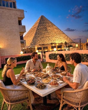 Eine Gruppe speist im Freien, mit einer Pyramide im Hintergrund.