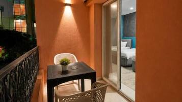 A balcony with a table and chairs, a potted plant, and a sliding glass door leading to a room.