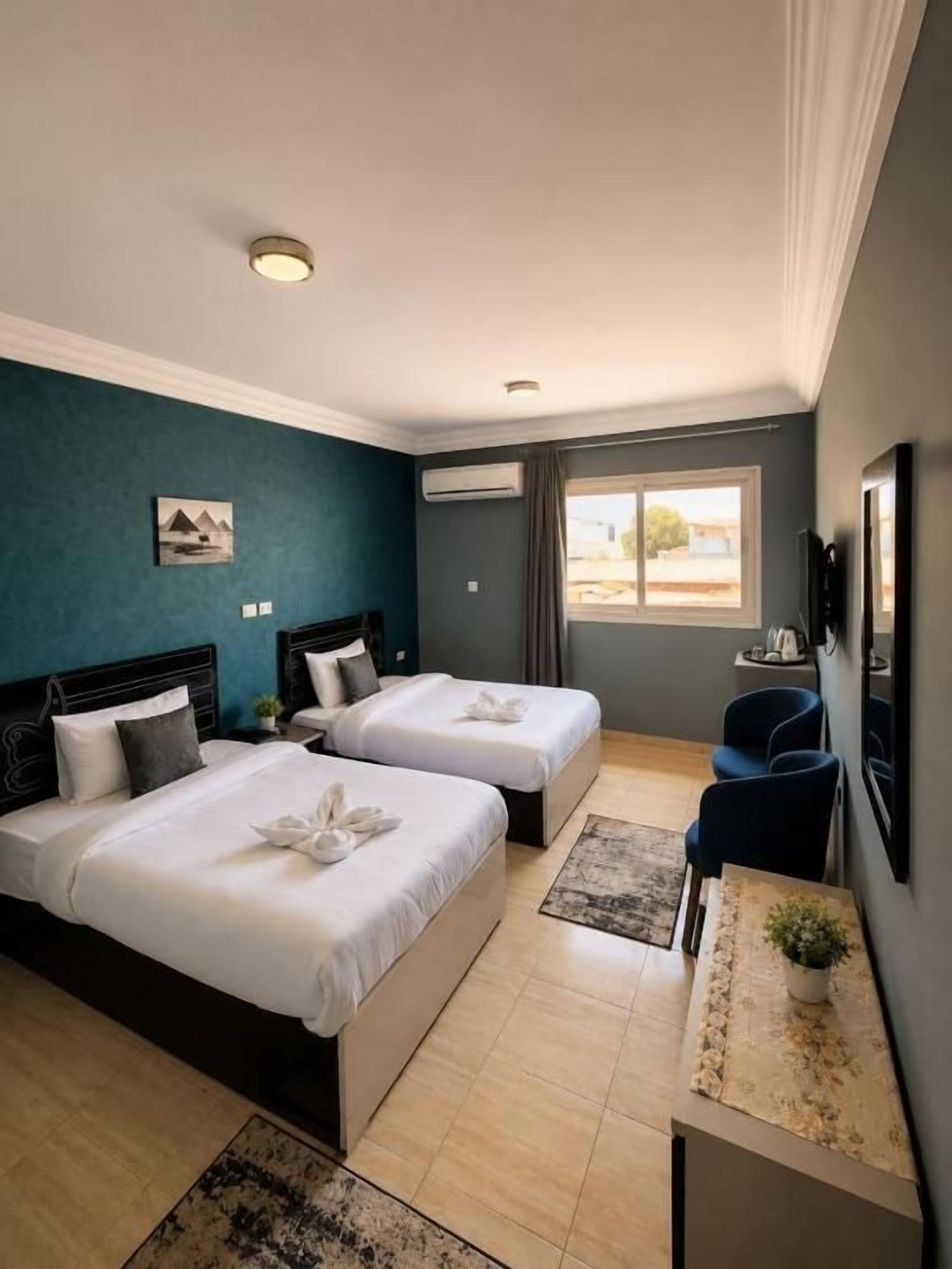 A hotel room with two beds, a desk, a chair, a TV, and a window with a view.