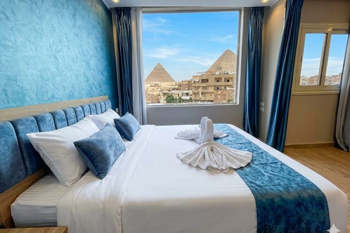 A hotel room with a bed, a view of pyramids, and curtains.