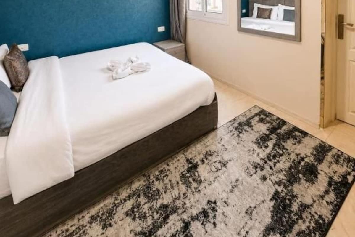 Ein Schlafzimmer mit einem Bett, einem Nachttisch, einem Spiegel und einem Fenster.
