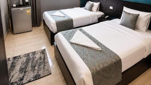 Quarto de hotel com duas camas, uma escrivaninha, mini-geladeira e janela com cortinas.