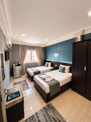Ein Hotelzimmer mit zwei Betten, einem Schreibtisch mit Computer, einem Kleiderschrank und einem Fenster mit Vorhängen.