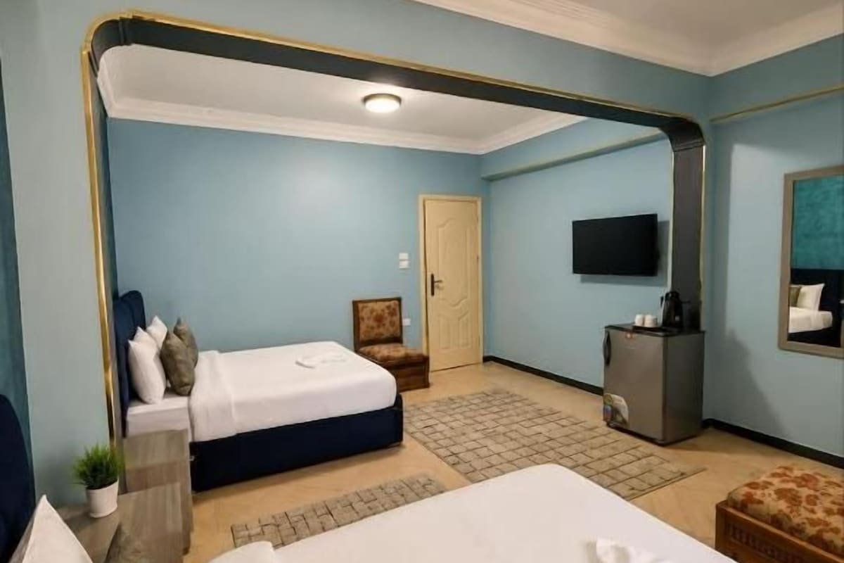 Ein Hotelzimmer mit einem großen Bett, einem kleineren Bett, einem Schreibtisch, einem Fernseher und einer Tür zu einem anderen Raum.