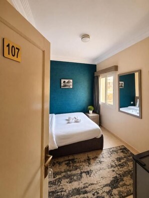 A hotel room with a bed, a bedside table, a mirror, and a door marked with the number 107. - Beko Pyramids Inn (Giza)