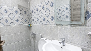 A bathroom with a shower, toilet, and sink, featuring speckled tiles and a mirror.