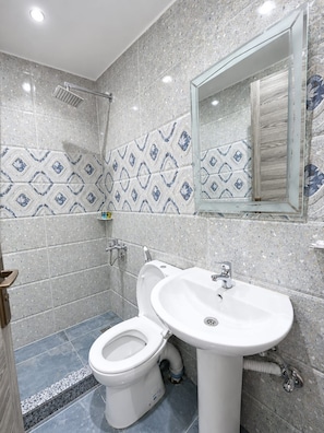 A bathroom with a shower, toilet, and sink, featuring speckled tiles and a mirror.
