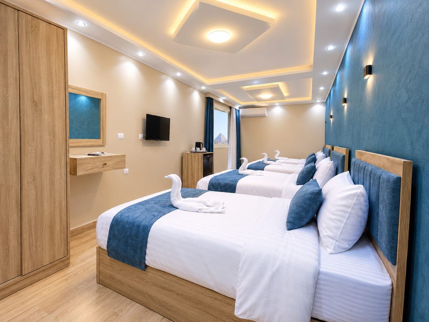 Habitación de hotel con dos camas, televisor, escritorio y vista a la ciudad.