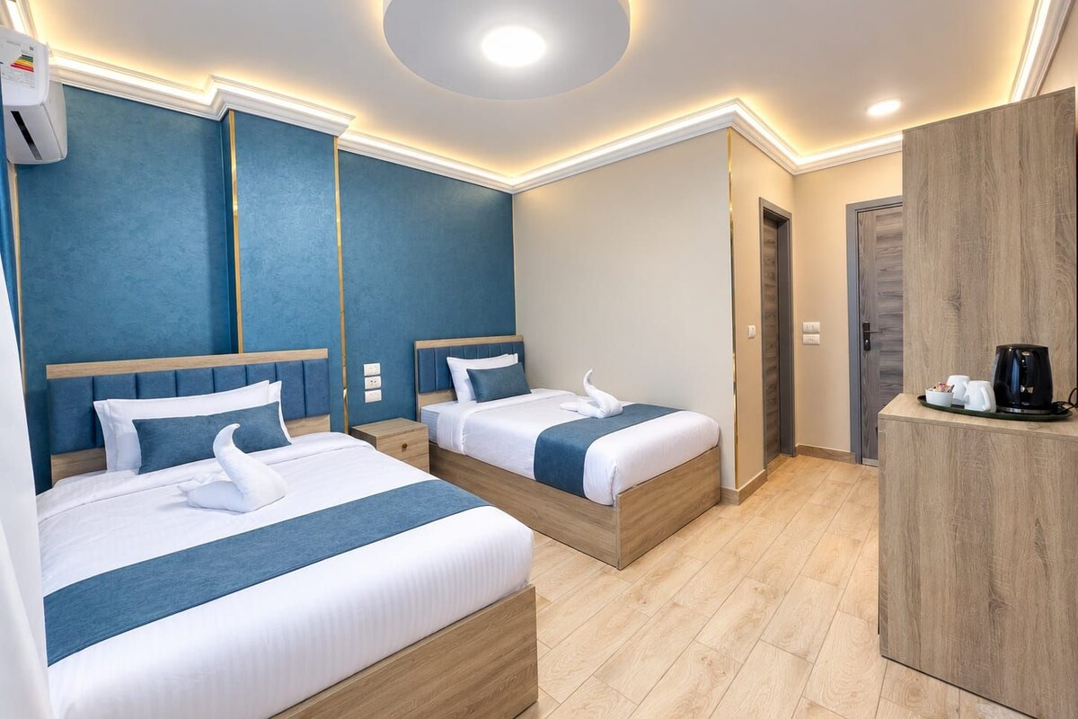 A hotel room with two beds, a wooden wardrobe, and a coffee station.