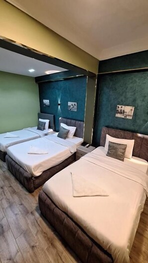 A hotel room with two beds, a wooden floor, and a green accent wall. - Beko Pyramids Inn (Giza)