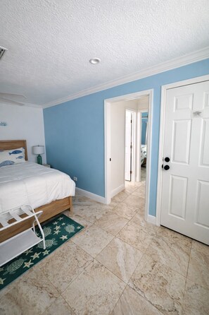 A bedroom with a bed, a nightstand, a lamp, a door, and a hallway leading to another room. - Suite Escape - Waterfront Paradise with Private Dock (Marathon)