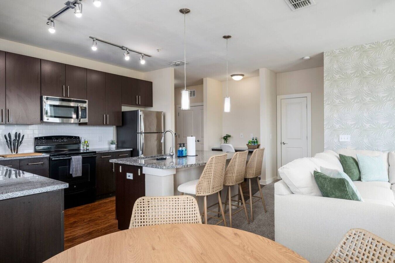 Una cocina moderna con armarios oscuros, electrodomésticos de acero inoxidable y una isla central con taburetes de bar.