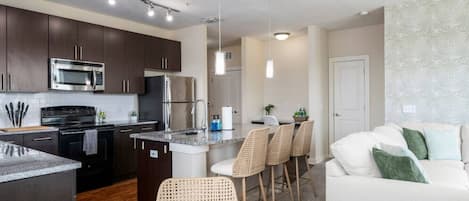 Una cocina moderna con armarios oscuros, electrodomésticos de acero inoxidable y una isla central con taburetes de bar.