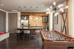 A modern kitchen with a herringbone-patterned backsplash, a central island with bar stools, and a foosball table. - Palm Luxury Huge 2br/2ba Pool/Gym Downtown Tampa (Tampa)