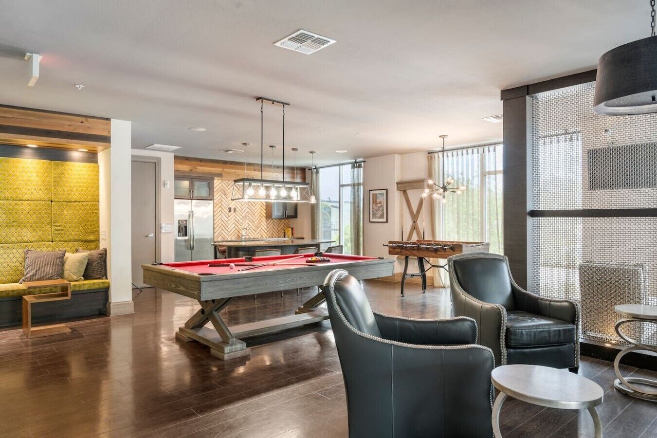 A modern living room with a pool table, leather chairs, and a kitchen area in the background.