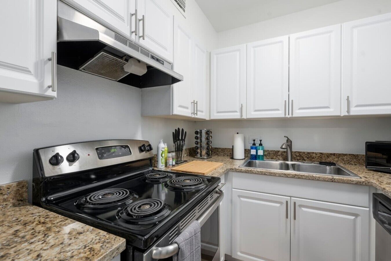 A kitchen with white cabinets, a black stove, granite countertops, and a stainless steel sink.