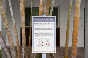 A signboard with instructions for playing bocce ball, placed in front of a building with bamboo pillars.