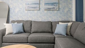 En grå modulsofa med flere puder, et rundt træsofabord og en væg med et blomstermønster samt to indrammede kunstværker.