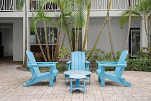 A patio area with blue Adirondack chairs and a small round table, surrounded by palm trees and a building with white walls and balconies. - 2BR Downtown Tampa Resort Retreat with Pool (Tampa)