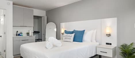 A modern hotel room with a bed, bedside tables, a nightstand, a desk, and a mirror.