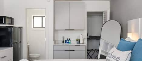 Un dormitorio con cama, mesita de noche, armario y baño visible a través de una puerta abierta.