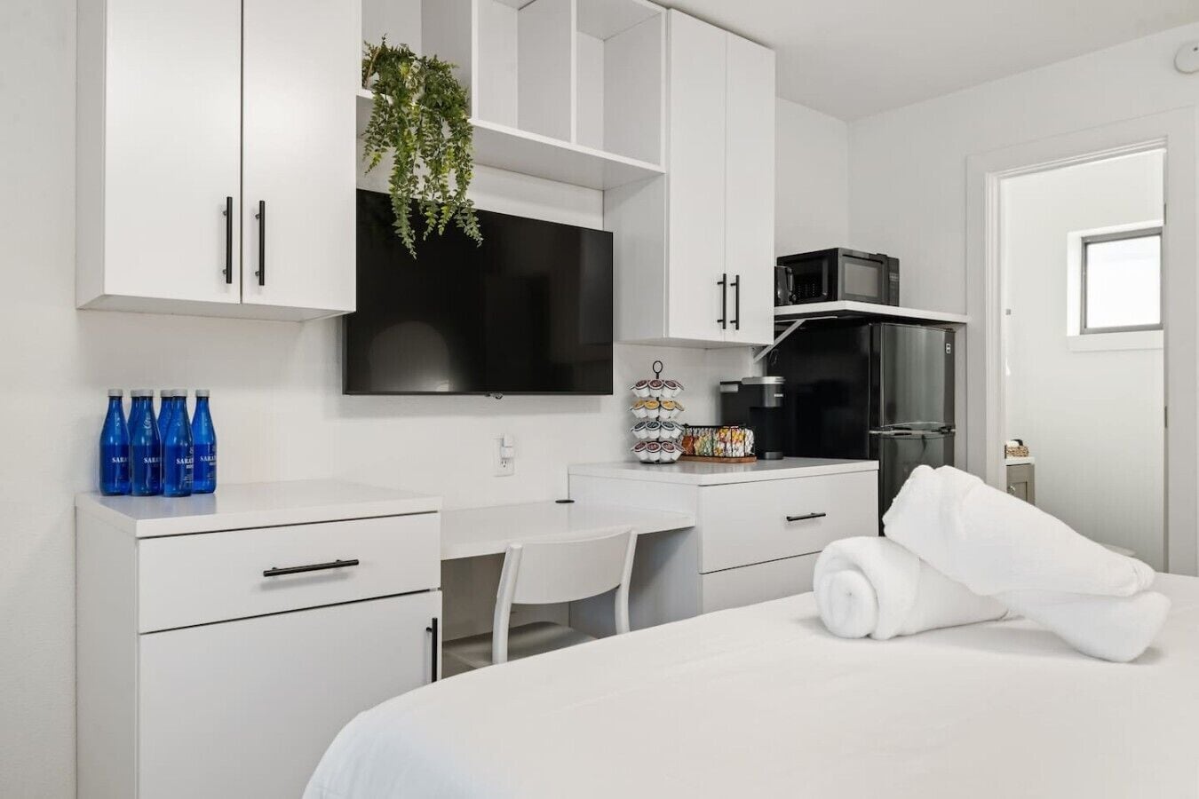 A modern hotel room with a bed, a desk, a television, a microwave, and a refrigerator.
