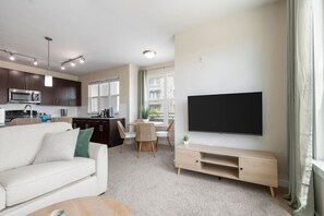A modern living room with a flat-screen TV, a sofa, a dining area with chairs, and a kitchen with dark cabinets and a microwave. - Luxury Palm Retreat - HUGE 2BR 2BA near Downtown (Tampa)