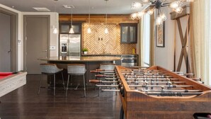 A modern kitchen with a herringbone-patterned backsplash, a central island with bar stools, and a foosball table. - Luxury Palm Retreat - HUGE 2BR 2BA near Downtown (Tampa)