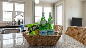 A kitchen area with a basket containing two bottles of Pellegrino water, a bag of PopCorners, and a wicker chair. - Luxury Palm Retreat - HUGE 2BR 2BA near Downtown (Tampa)