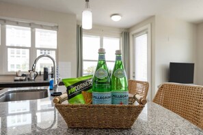 Eine Küchenzeile mit einem Korb, der zwei Pellegrino-Flaschen, eine Tüte PopCorners und einen Korbstuhl enthält.