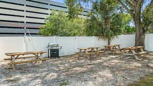 An outdoor patio area with picnic tables, a barbecue grill, and a white fence. - Cozy Studio: BBQ, Dining & Relaxing Vibes (Tampa)
