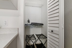 A white closet with a hanging rack, a shelf with folded clothes, and a power outlet. - UTampa - Downtown Studio Next to UT and Riverwalk (Tampa)