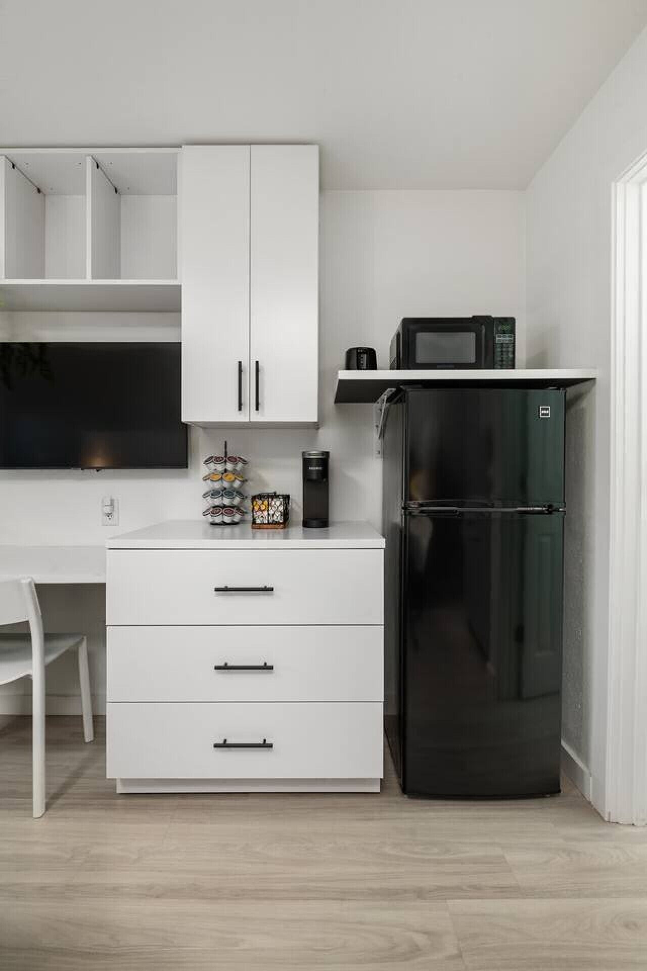 A compact kitchen with a white cabinet, a black refrigerator, and a microwave on the countertop.