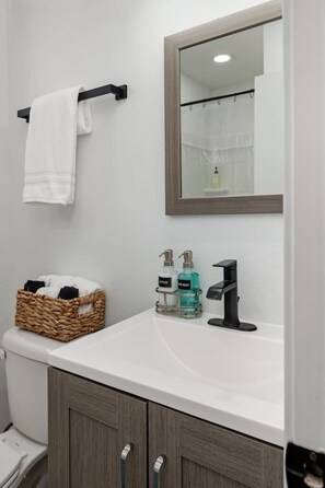 A bathroom with a white sink, a mirror, a towel rack, a basket, and two soap dispensers. - Stylish Studio w/ BBQ & Outdoor Oasis (Tampa)