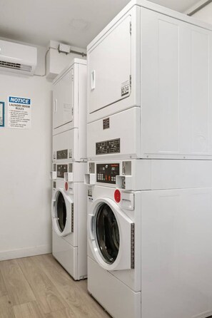 A laundry room with two stacked front-loading washing machines, a notice board with laundry room rules, and a control panel on the machines. - Stylish Studio w/ BBQ & Outdoor Oasis (Tampa)