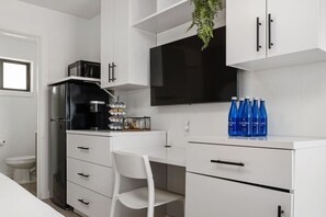 A modern kitchen with white cabinetry, a black refrigerator, a coffee maker, and a flat-screen TV. - Stylish Studio w/ BBQ & Outdoor Oasis (Tampa)