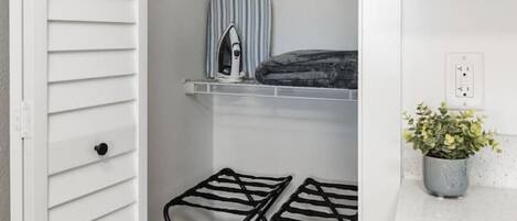 A closet with a hanging rack, a shelf with a striped item, and a potted plant on a countertop.