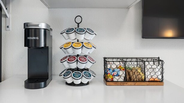 A kitchen with a coffee maker, a tiered container of coffee pods, and a wire basket with food items. - Stylish Studio w/ BBQ & Outdoor Oasis (Tampa)