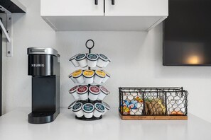 A kitchen with a coffee maker, a tiered container of coffee pods, and a wire basket with food items. - Stylish Studio w/ BBQ & Outdoor Oasis (Tampa)