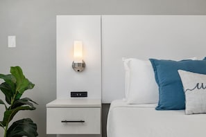 A bedroom with a bedside table, a nightstand, a wall-mounted light, a bed with pillows, and a plant. - Stylish Studio w/ BBQ & Outdoor Oasis (Tampa)