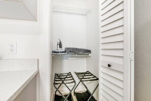 A laundry area with a hanging rack, an ironing board, and a shelf with folded clothes.