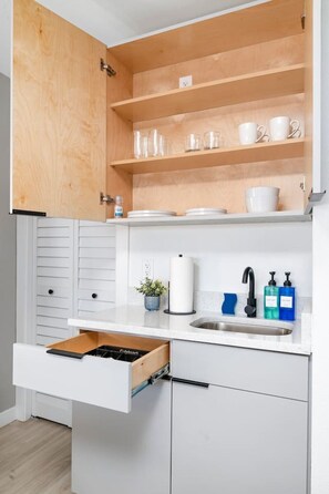 A compact kitchen with a built-in shelf, a sink with a faucet, and a countertop with a dish soap dispenser.