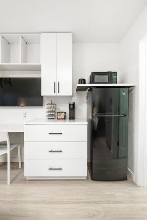 A compact kitchen with white cabinetry, a black refrigerator, and a microwave on the countertop.