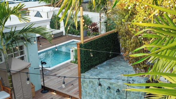 En swimmingpool med træterrasse, omgivet af tropiske planter og et hvidt telt.