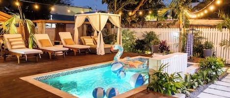 Un espace piscine aménagé avec des chaises longues, un auvent et une petite piscine gonflable avec des ballons de plage.
