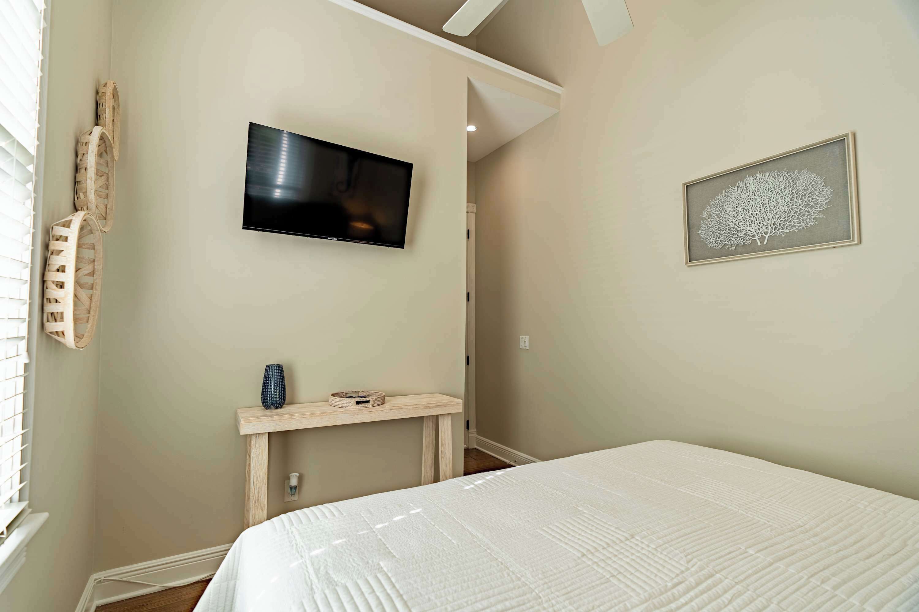 A bedroom with a bed, a television mounted on the wall, a small table with a vase, and a framed artwork on the wall.