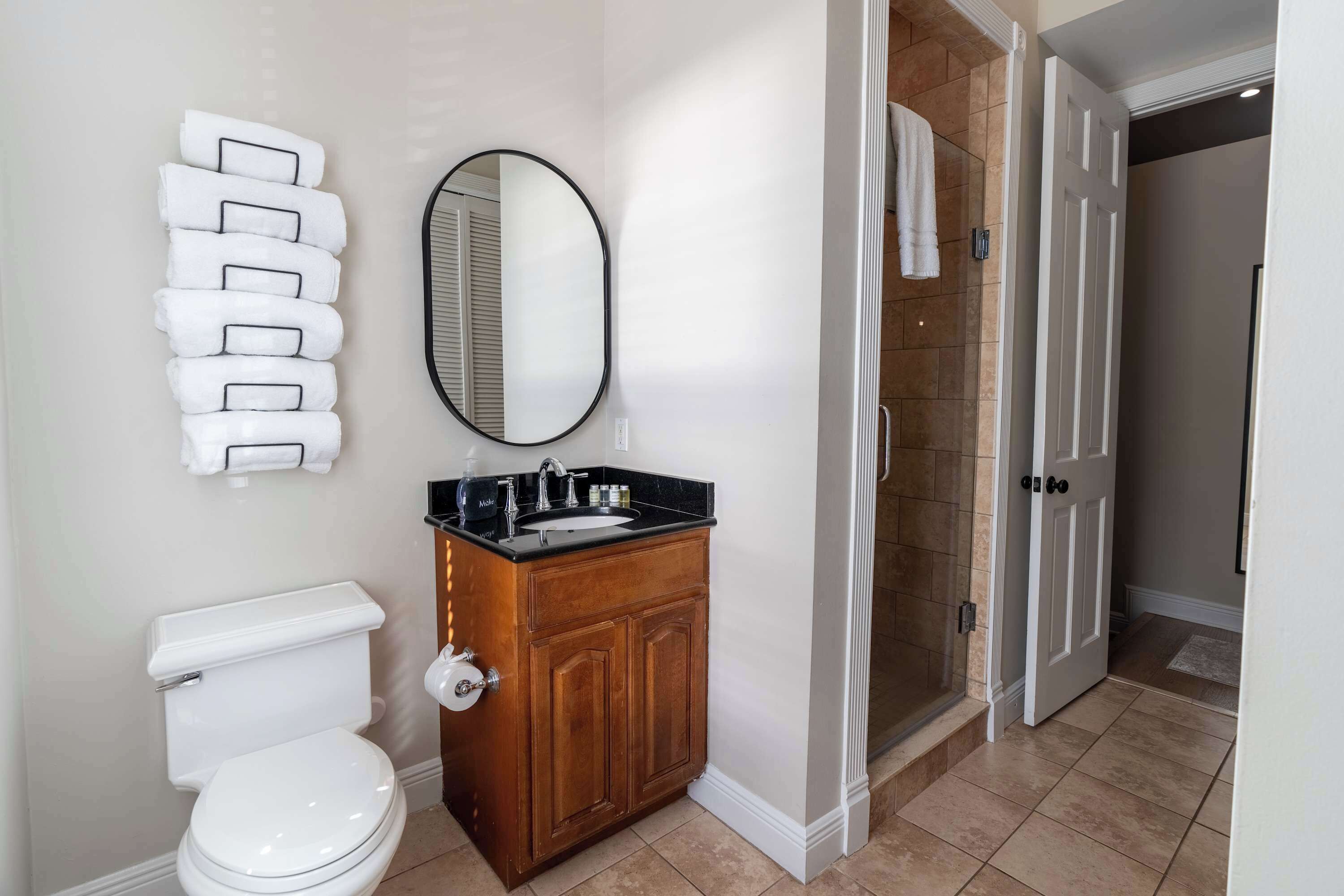 Een badkamer met een toilet, een houten wastafelmeubel met een wastafel, een spiegel en een handdoekhouder.