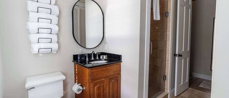 Een badkamer met een toilet, een houten wastafelmeubel met een wastafel, een spiegel en een handdoekhouder.