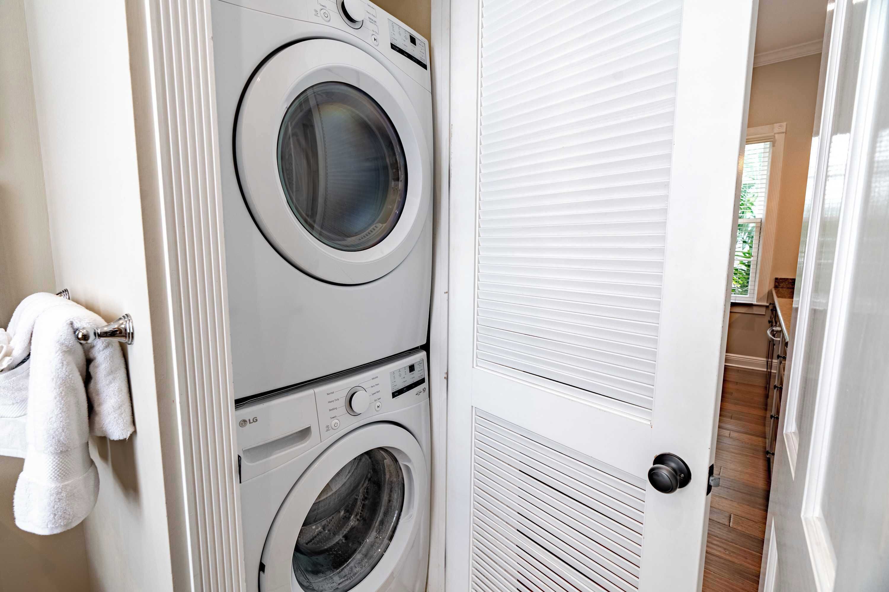 Un lavadero con dos lavadoras apiladas y una puerta que da a un pasillo.