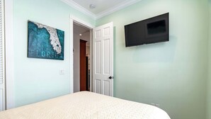 Quarto com cama, televisão na parede e porta para outro cômodo.